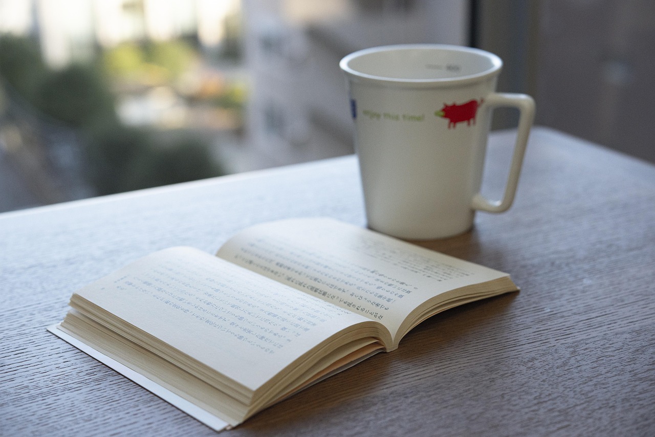 A white porcelain mug and an opened book on a wooden table.